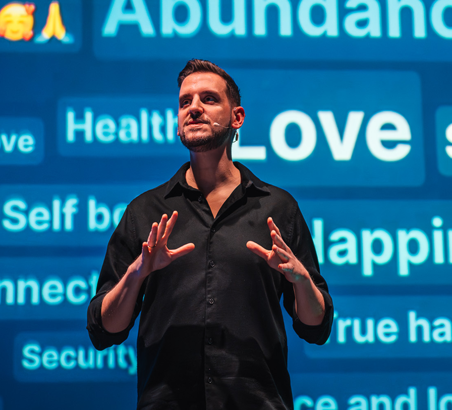 Alexis Alcalá mid-keynote in front of a wall of words: Abundance, Peace, Love, Joy, Health, Self love, True happiness