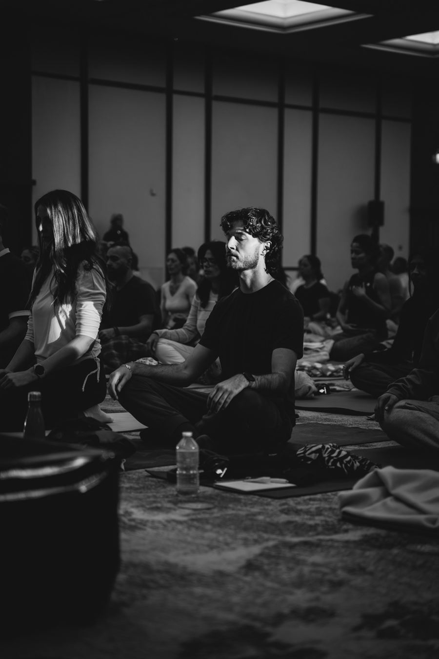 Black-and-white close-up of Alexis seated in lotus pose in a meditation circle