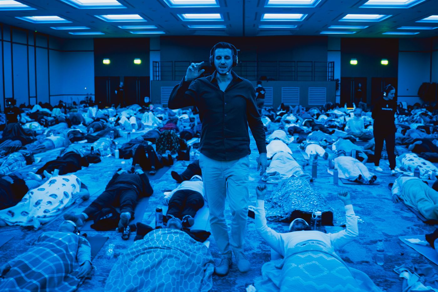 Alexis walking through a sea of participants lying on the floor in blue ambient light