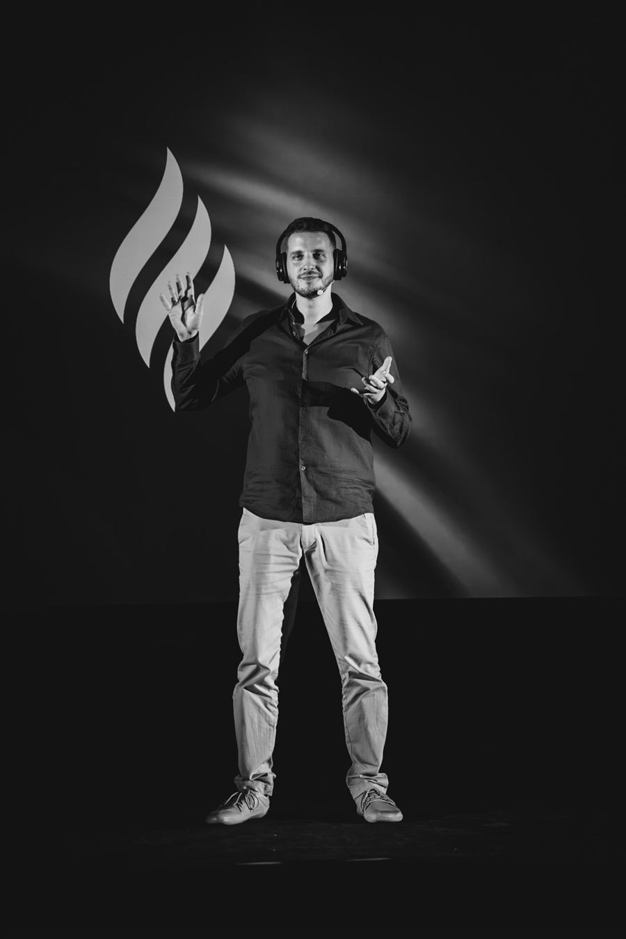 Black-and-white full-body shot of Alexis on stage with the InnerCamp flame logo behind him